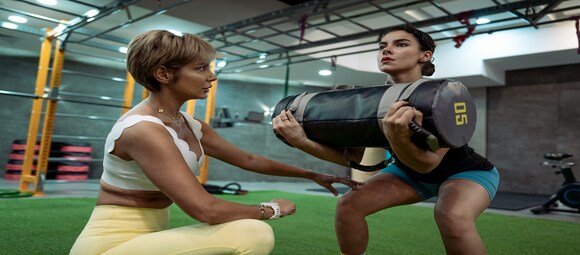 Coach sportive accompagnant une femme pendant un squat avec sac de sable en salle de sport