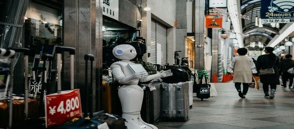 **Balise ALT optimisée :**
`Robot humanoïde blanc devant une boutique dans une rue commerçante japonaise animée, symbolisant l’intelligence artificielle et le commerce urbain`